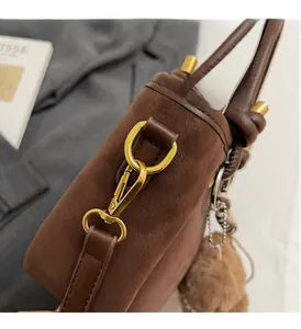 Detail der braunen Wildleder-Schultertasche mit goldenen Beschlägen und Plüschanhänger