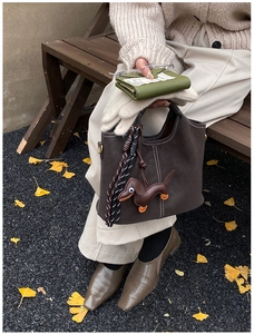 Close-up of brown suede handbag with white stitching and leather dachshund charm