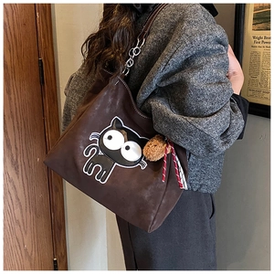 Détail d'un cabas en daim marron avec écusson de chat et pendentif ours en peluche