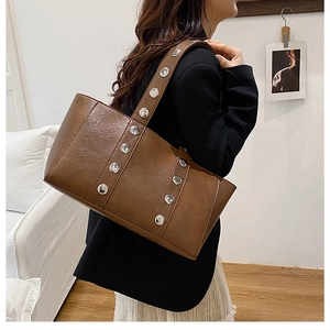 Grand sac cabas marron avec rivets argentés porté par un mannequin en veste noire