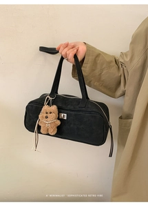 Detalle de bolso bowling de ante negro con cierre giratorio plateado y colgante de oso