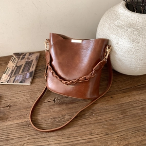 Detailed view of a vintage brown leather bucket bag with a woven handle on a wood surface