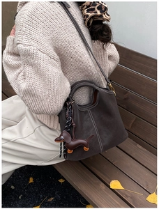 Detail of dark brown matte bucket bag with white contrast stitching and dog charm