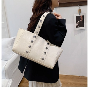 Gros plan du sac porté épaule beige avec clous argentés et texture cuir grainé