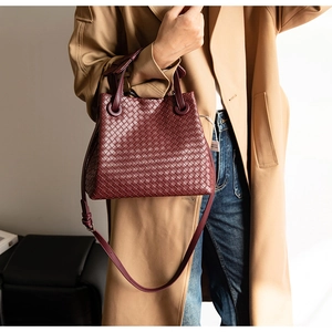 Detail of burgundy woven leather bucket bag featuring a detachable crossbody strap