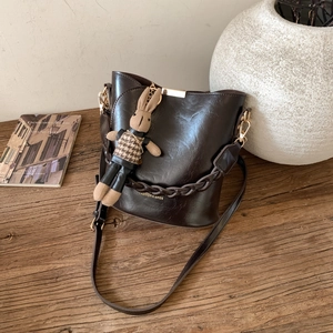 Close-up of brown vintage bucket bag featuring a knit rabbit charm and woven chain handle