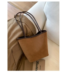 Detailed view of brown suede bucket bag with dark coffee leather trim on a cozy background