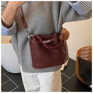 Detail of burgundy leather bucket bag with woven handle and brown plush bear charm