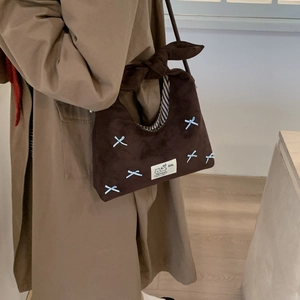 Close-up of brown suede shoulder bag with blue bow embroidery and cat label detail