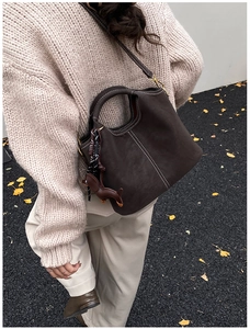 Detail of dark brown matte bucket bag with white stitching and dachshund leather charm