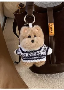 Détail d'un bijou de sac chien en peluche avec pull rayé et médaillon gravé sur un sac