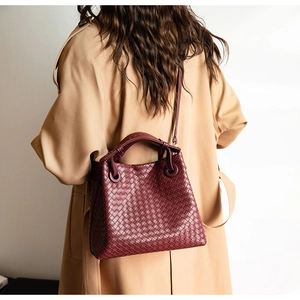 Detailed view of burgundy woven leather bag on khaki trench coat with crossbody strap