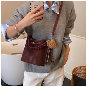 Detail of wine red leather bucket bag with braided handle and cute plush bear charm