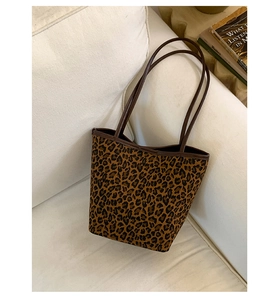 Detail of a large leopard print tote bag with brown leather handles on a beige sofa