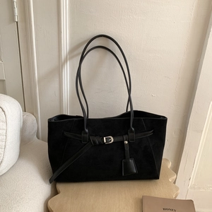 Close-up of black matte suede tote bag with decorative strap buckle and leather tag