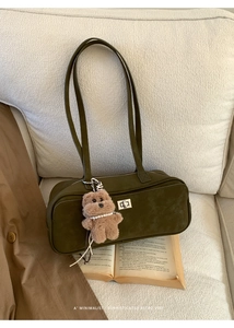 Detalle de bolso de hombro de ante verde oliva con cierre giratorio plateado y oso de peluche