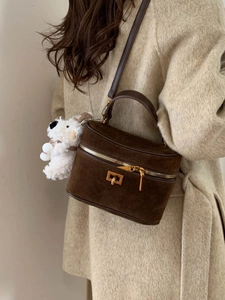 Sac boîte en daim marron avec fermoir doré et charme peluche sur un manteau beige