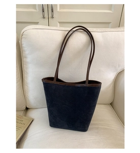 Close-up of a blue suede bucket bag with brown leather straps on a beige sofa