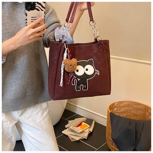 Détail du sac cabas en toile bordeaux avec écusson de chat et charme d'ours en peluche