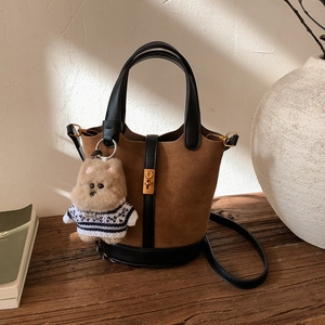 Détail du sac seau en daim marron avec fermoir doré tournant et un petit ours en peluche