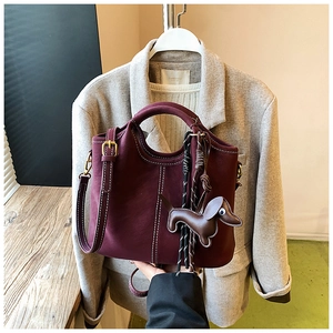 Detail of burgundy leather bucket bag with white contrast stitching and a dog charm