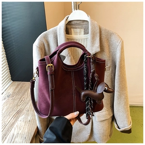 Detail view of burgundy leather handbag with white contrast stitching and a dog-shaped charm