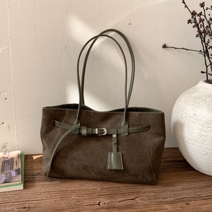 Detail of olive green suede tote bag with decorative buckle on a rustic wooden bench