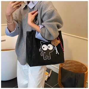 Détail du sac cabas en toile noire avec motif de chat de dessin animé et charm d'ours