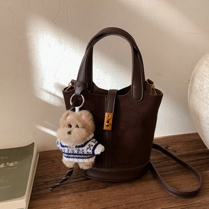 Détail du sac seau marron foncé en daim et cuir avec charm ours en peluche sur table bois