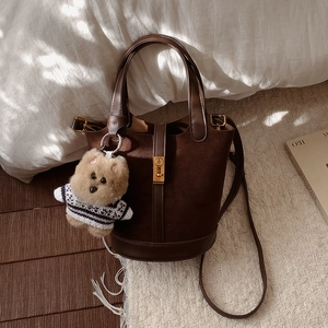 Détail d'un sac seau en daim marron avec fermoir doré et un pendentif chien peluche
