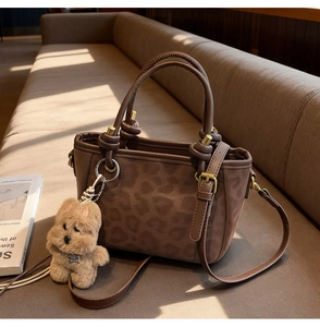Détail du sac à main imprimé léopard avec pendentif chien en peluche sur un sofa