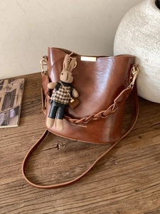 Brown vintage leather bucket bag with gold clasp and cute rabbit charm on wood background