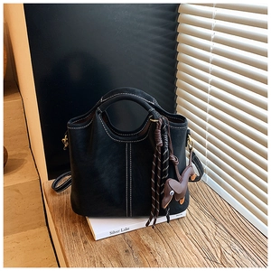 Detail view of black matte bucket bag with white stitching and dachshund charm