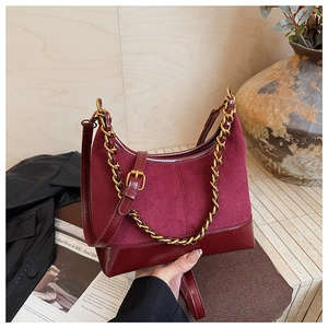 Close-up of wine red suede and patent leather bag with chunky gold chain detail