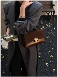 Close-up of vintage brown shoulder bag with golden S-buckle and mixed leather textures