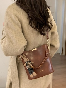 Brown bucket bag with woven handle and cute rabbit charm on a beige coat background