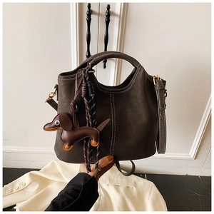 Detail of dark brown matte leather bag with white contrast stitching and puppy charm