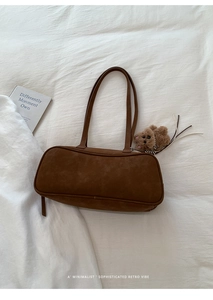 Bolso de hombro en ante marrón oscuro con colgante de oso sobre fondo de tela blanca