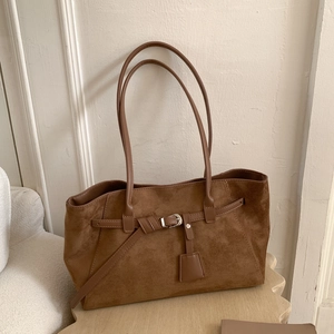 Close-up of brown suede tote bag with metal buckle and leather strap on a wooden stand