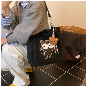 Détail de broderie de chat sur cabas en toile noire avec chaîne et pendentif ours en peluche