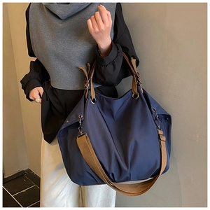 Detail of navy blue large canvas tote bag featuring brown woven strap and side metal ring