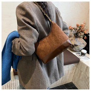 Detail of a brown patchwork crescent bag with a gold chain strap on a blazer outfit