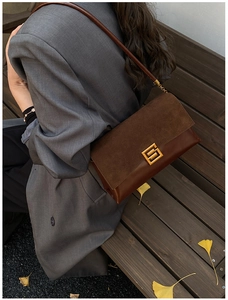 Detail of dark brown leather shoulder bag with gold clasp and autumn foliage background