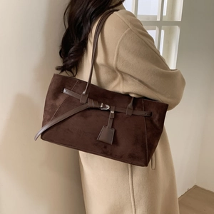 Detail of dark brown suede tote bag featuring silver buckle and strap on beige coat