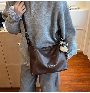 Detail of dark brown leather crossbody bag with a cute plush dog and leopard bow charm
