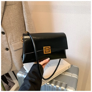 Detail of a black leather shoulder bag featuring a geometric gold buckle on a suit background