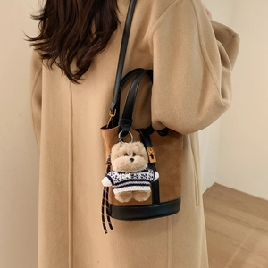 Détail du sac seau en daim avec pendentif ours Top Dog porté à l'épaule par le mannequin