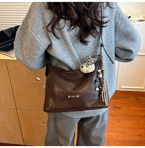 Detail of dark brown leather hobo bag with vintage metal logo and plush dog charm