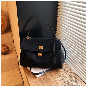 Detail of black suede tote bag with gold twist locks and leather handle on wooden table