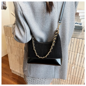 Detail of black suede and patent leather bag with a chunky gold chain strap